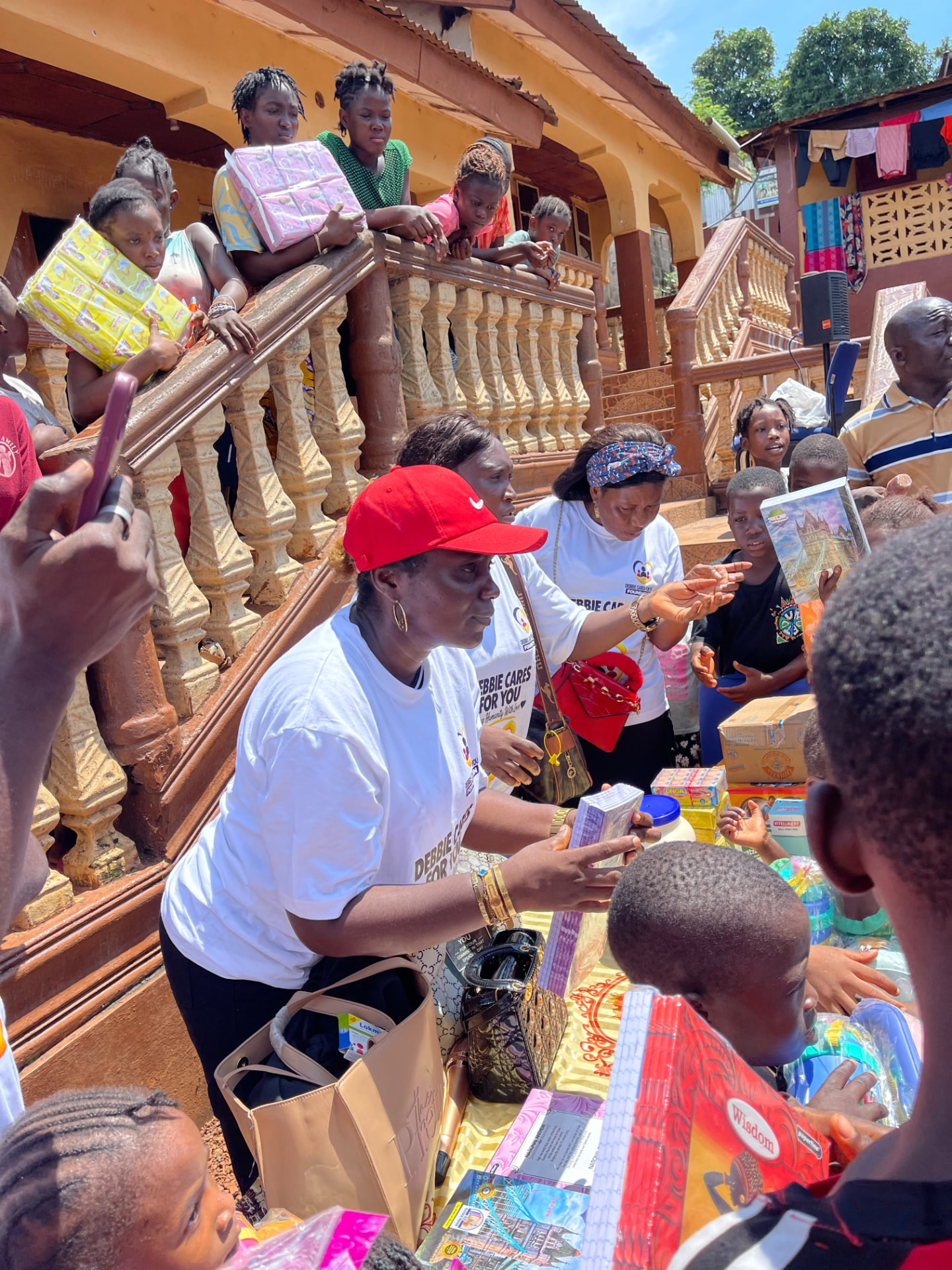 A volunteer in a red cap hands a new book to a child while others look on from the stairs